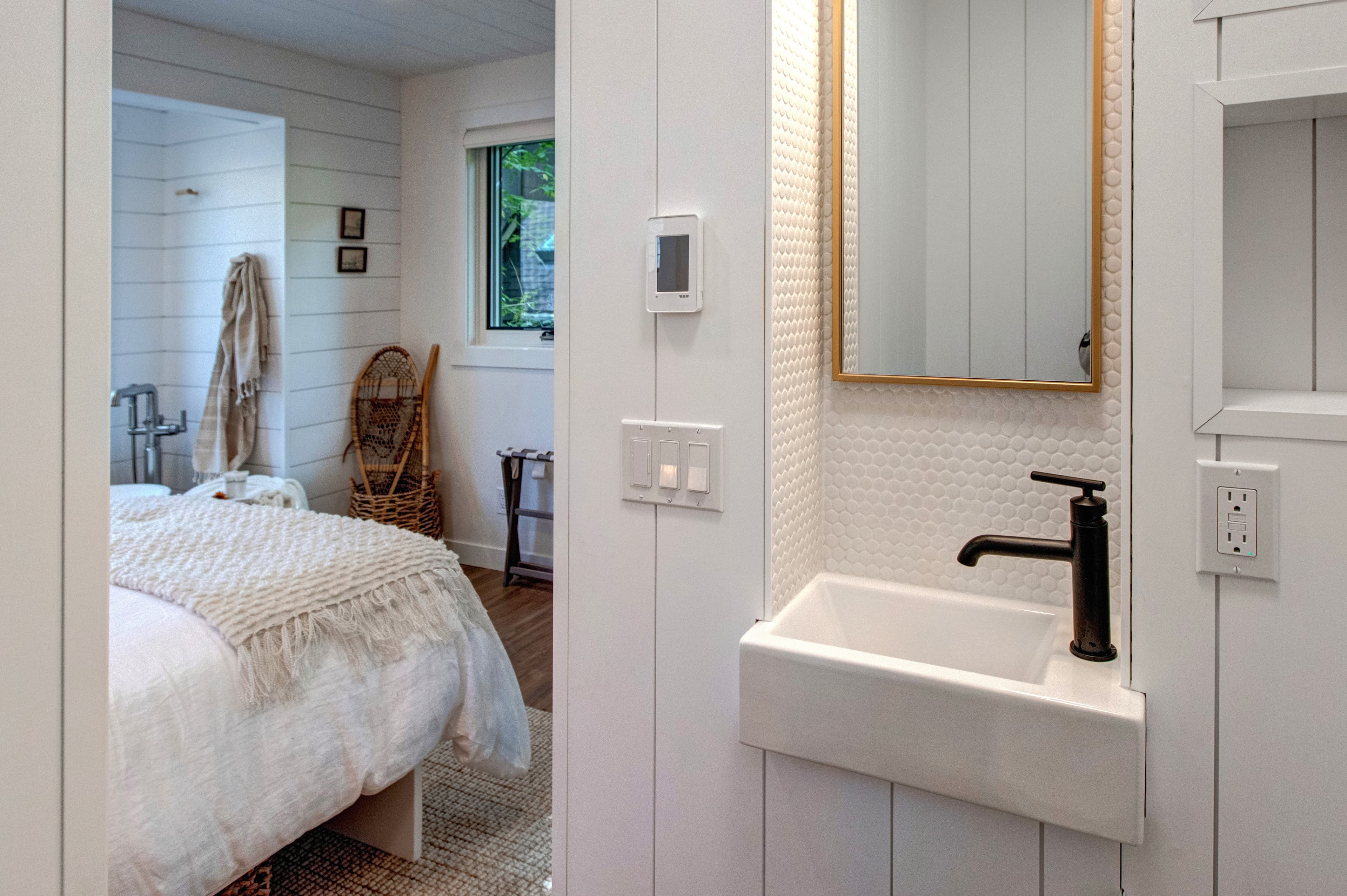 Lofted bedroom in detached guest suite, with a queen bed next to standalone bathtub and half bathroom.